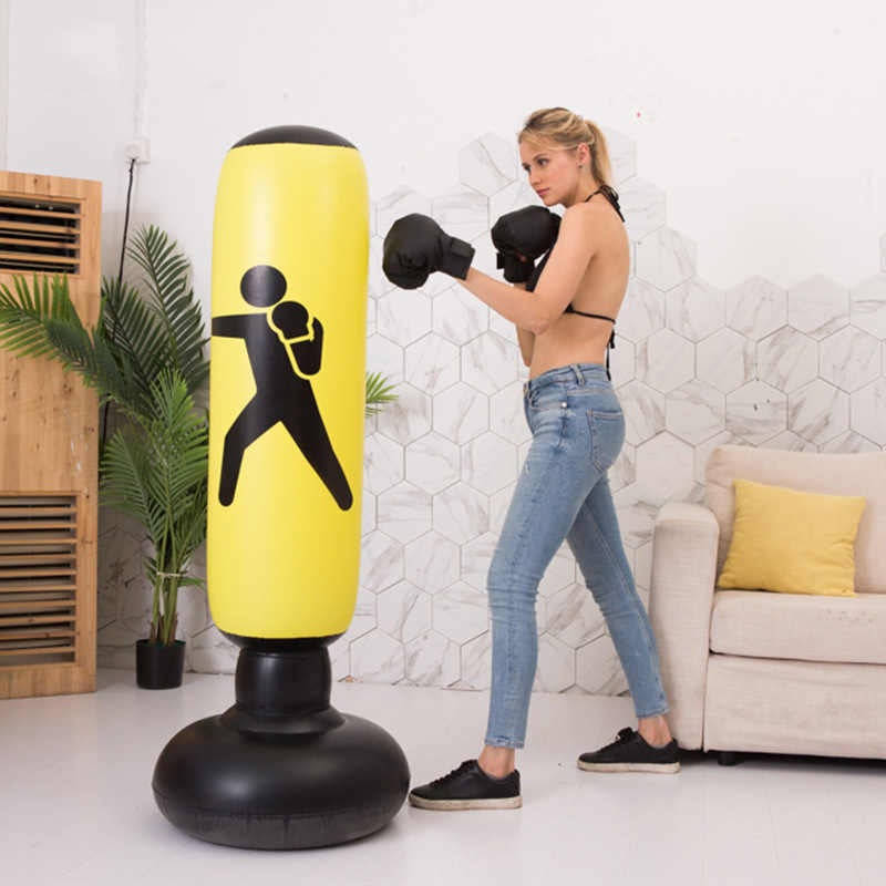Woman practicing boxing on a yellow punching bag in a living room.