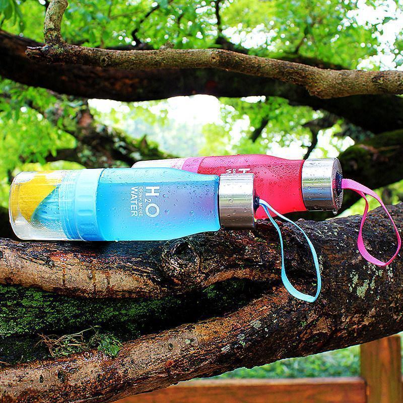 Colorful water bottle with a straw on a tree branch outdoors